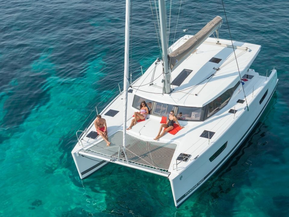 Aerial view of a catamaran with guests on the forward trampolines over blue-green water