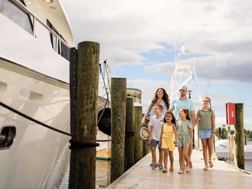 Family walking along a marina dock beside a yacht