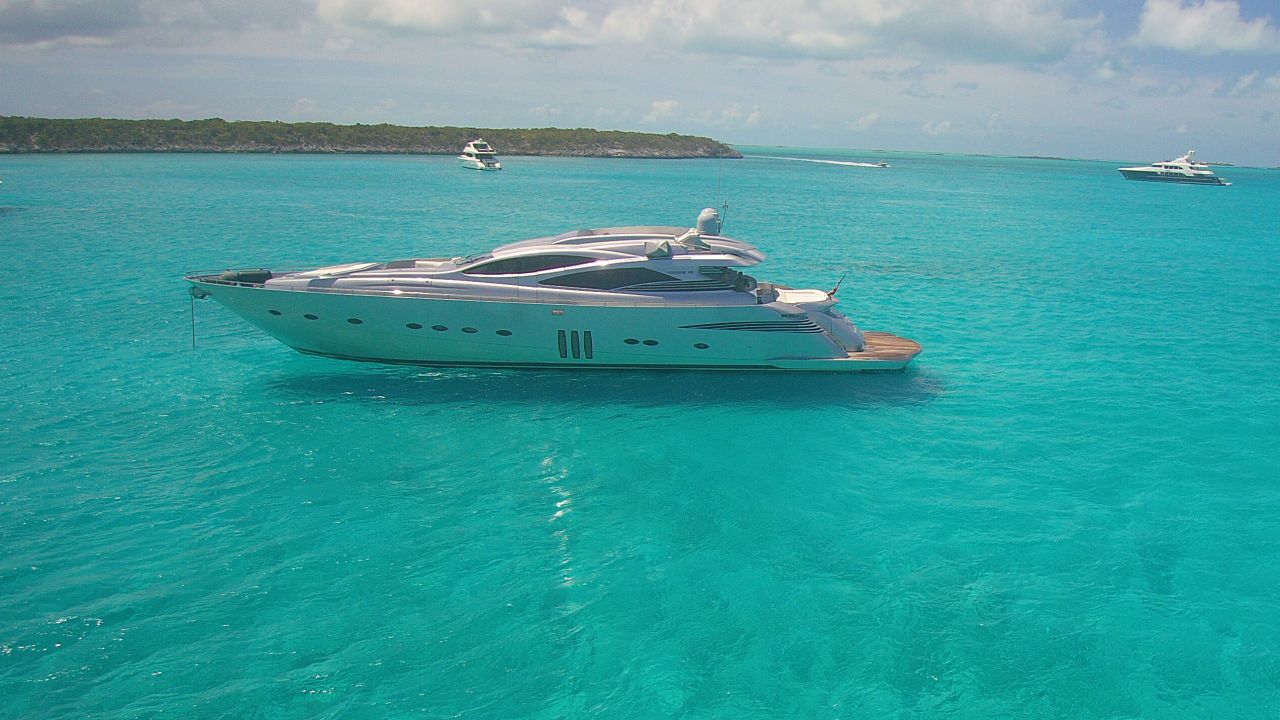 Sleek luxury sport yacht anchored on vivid turquoise water near a low green coastline