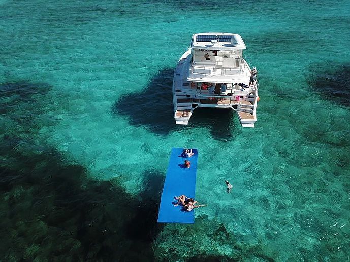 Aerial view of a power catamaran at anchor with a floating mat in turquoise water