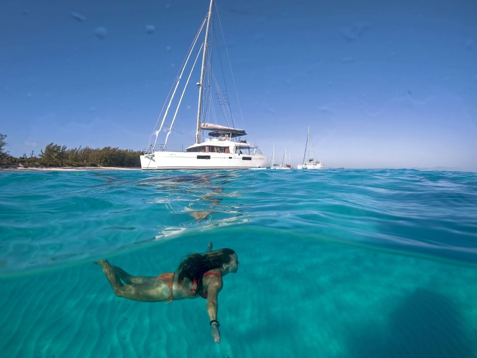 Swimmer diving below a catamaran anchored in clear blue water