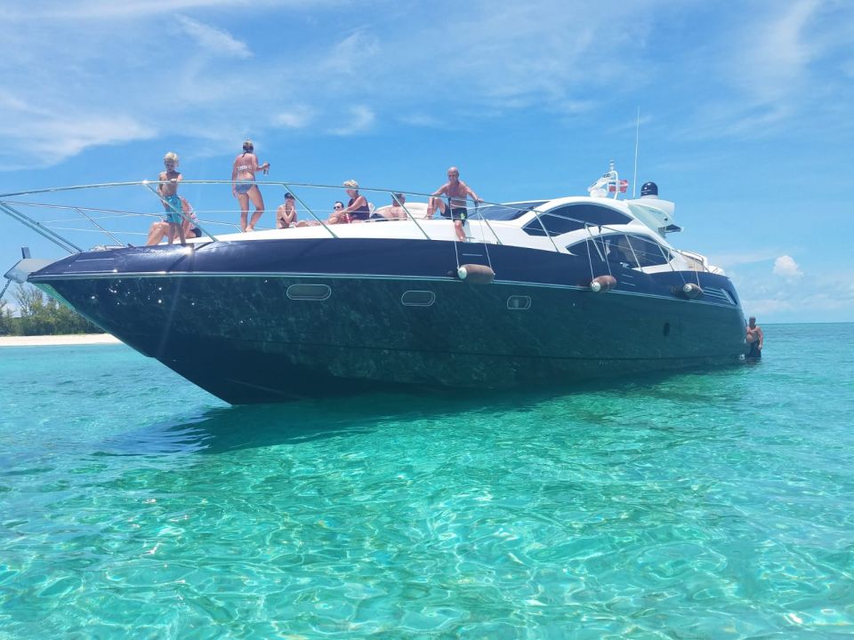 Group of guests standing on the foredeck of a dark-hulled sport yacht in turquoise shallows