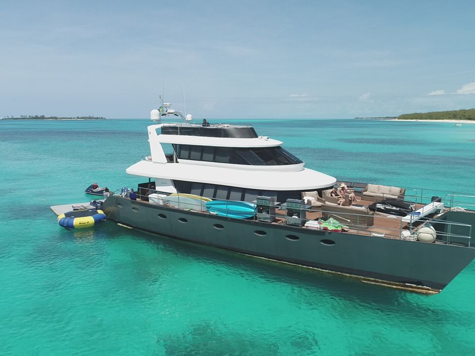 Large motor yacht at anchor over teal water with a tender and floating platform nearby