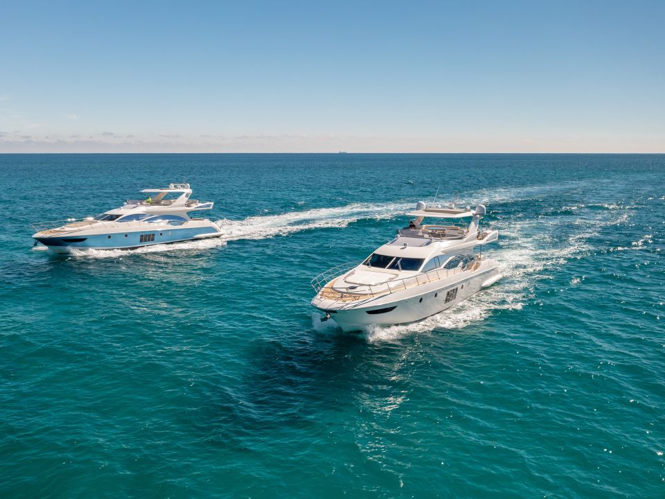 Two flybridge motor yachts cruising across blue water