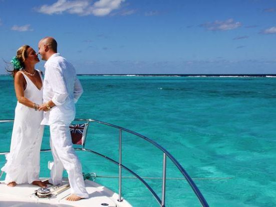 Newlywed couple embracing on the bow of a yacht above turquoise water